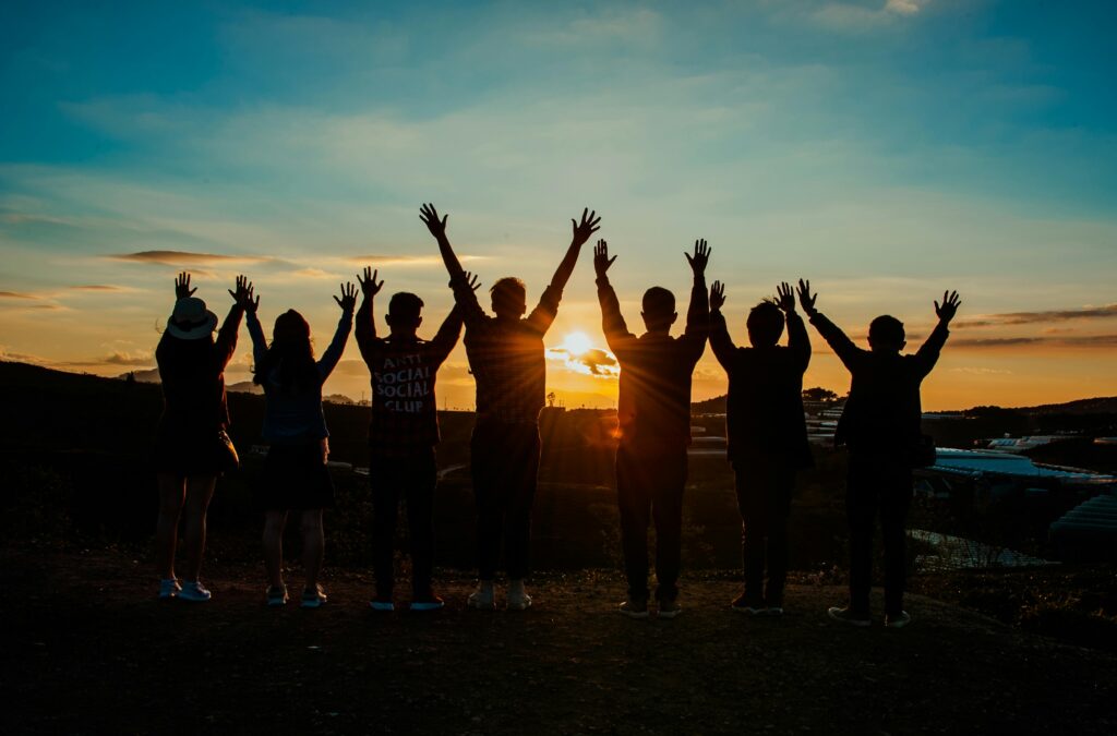 A diverse group of friends raises their arms in celebration against a vibrant sunset backdrop.